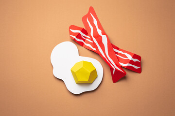Paper craft food on beige or light brown background. Fried eggs and bacon slices cut from paper,...