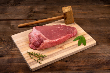 Topside steak on bamboo board with salvia and rosemary on wooden background