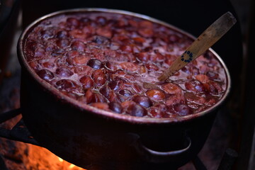 cooking plum jam in a traditional style with firewood. boiling the fruit outside in a large...