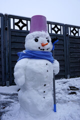 ein Schneemann mit Schal, Besen und Eimer auf dem Kopf 