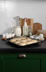 raw homemade yeast buns are ready for baking on the table with ingredients: milk, flour, eggs, oil