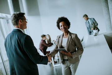 Businesswoman holding digital tablet and looking at handsome colleague while shaking hands in office