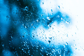 Raindrops on window glass in cold colors, tree branches in the background