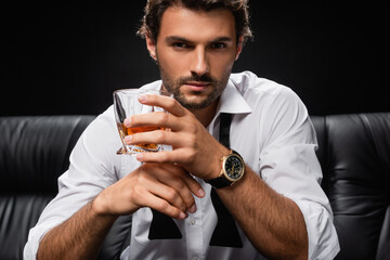man with glass of whiskey, in white shirt and untied tie, looking at camera isolated on black