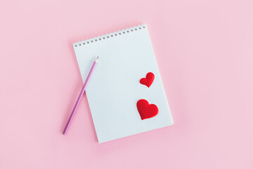 Notebook with blank page, pencil and red hearts on a pink background.