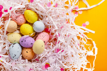 Easter composition with colored eggs lying in a nest of paper on a yellow background. Beautiful background and space for text