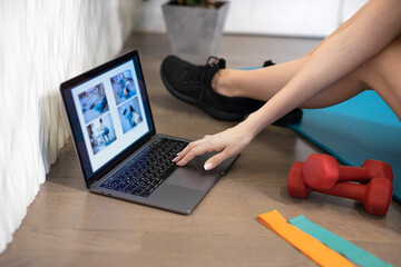 Young sporty slim woman preparing for online fitness training with modern laptop. Healthy lifestyle...
