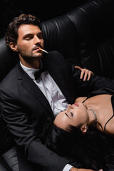 man with closed eyes smoking cigarette near sexy woman lying on his laps