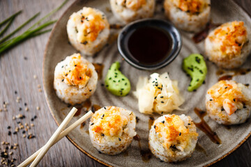 Baked sushi maki rolls with prawns and crab on a plate with chopsticks, soy sauce, wasabi and ginger. Japanese traditional fish food closeup served for lunch in modern gourmet restaurant