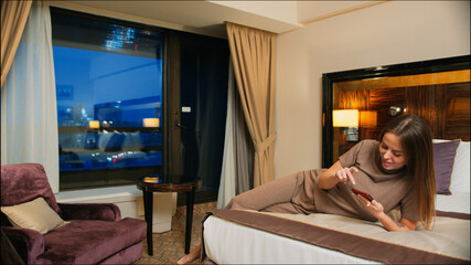 Attractive girl with phone on bed in hotel