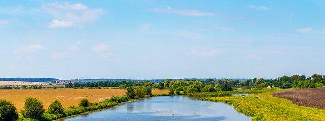 Summer landscape with river between fields. Wheat field and plowed field by the river. Panorama