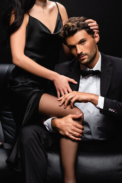 sexy woman in satin dress seducing elegant man in black suit isolated on black