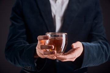 Midsection portrait of a man in a blazer holding a glass cup of tea