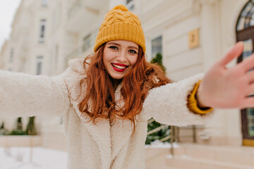 Carefree girl with long ginger hair making selfie in december morning. Outdoor photo of laughing...