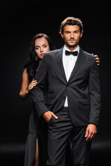 young confident man with hand in pocket near sensual brunette woman on black