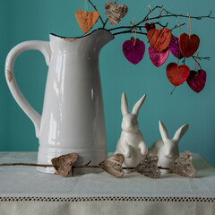 A twig with hearts in a jug and two porcelain hares