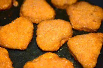 Breaded chicken nuggets are fried in a frying pan