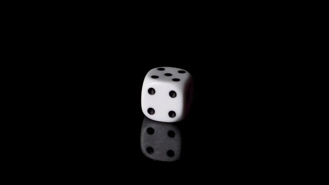 White dice rolls a five in slow motion, isolated on black background