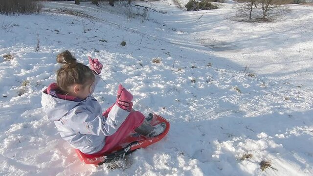 A young girl having winter fun sledging down a snowy hill in the sunshine