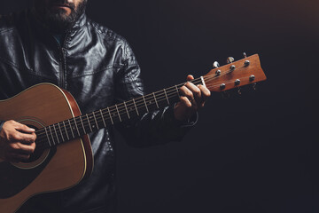 man in leather jacket playing an acoustic guitar on a black background