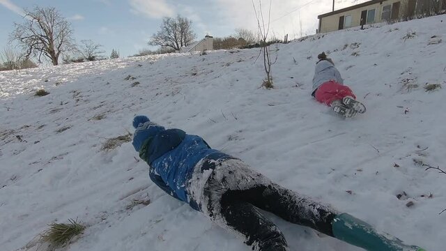 Children having fun in the snow with them rolling down in a playful manner. 