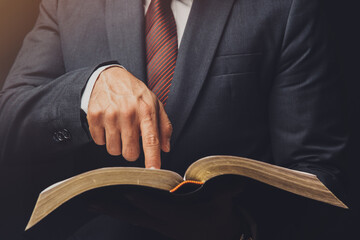 man in suit pointing a text on an open bible on a black background