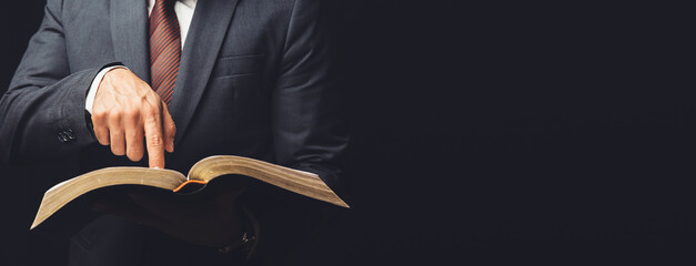 man in suit pointing a text on an open bible on a black background