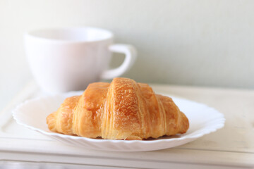 Croissant on white plate with coffee on the breakfast table in the morning, dessert at tea time break to relax