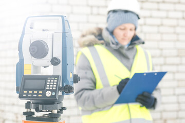 Fototapeta na wymiar a female engineer surveyor works with an electronic total station in winter, a tool for performing geodetic, construction and cadastral works on the ground, selective focusing, tinting.
