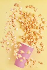 Flying delicious sweet popcorn with caramel in pink paper cup, isolated on trend color yellow background.