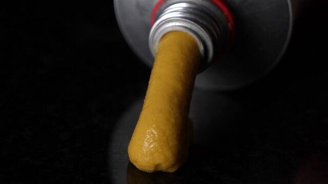 Close up pressing mustard out of a tube on black reflective table.