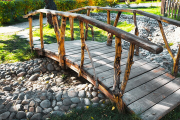 Fototapeta na wymiar A small decorative wooden bridge in the summer park is built over a dried-up stream. Lawn design ideas and landscape design.