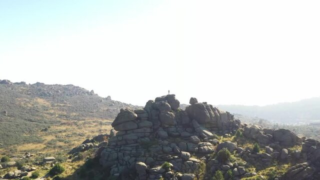 Young man perched on some rocks looking at the horizon in a natural park seen from a drone