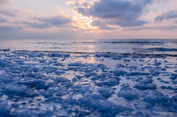 The frozen shore is covered with ice on the background of the sunset by the sea. Cold natural background