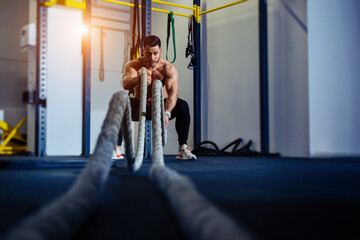 Young man with battle rope doing exercise in functional training fitness gym.