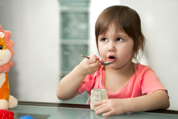 A little girl eats baby food from a glass jar. Copy space.