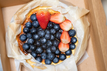 Pound of Basque Burnt Cheesecake with full fresh berries on top in paper craft box. Overhead shot.
