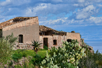 abandoned rural house on the coast of Eastern Sicily in the Province of Messina built on a promontory overlooking the sea with typical Mediterranean vegetation and succulents