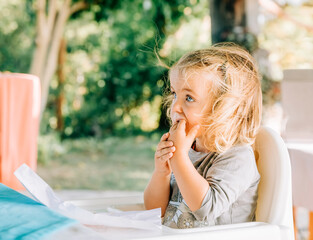 Girl sitting in high chair and biting on finger