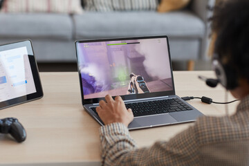 Back view close up of African-American boy playing video games online via laptop, copy space