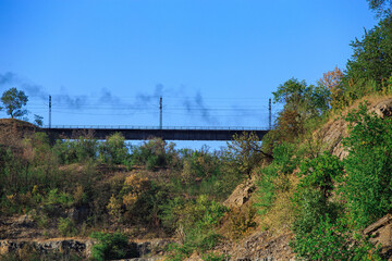 Fototapeta na wymiar Railroad bridge with smoke from a passing diesel locomotive in a mountainous area