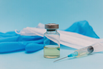 The vaccine is in a jar next to a syringe, a medical mask and blue gloves on a blue background