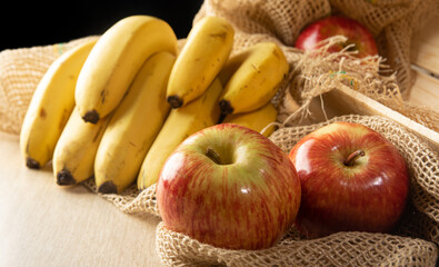 Apples and bananas, beautiful red apples and bananas on rustic wooden surface and rustic fabric, selective focus.