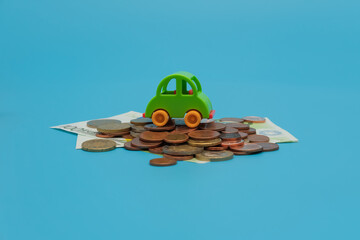 Green mini toy car on coins and banknotes on blue background. Buying car concept with copy space