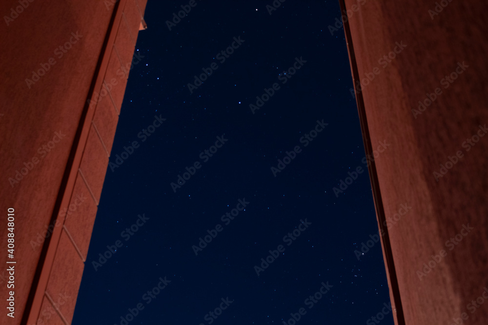 Wall mural a beautiful shot of starry city night sky in middle of two red walls with orion constellation. astro