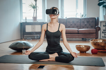Caucasian cheerful woman weared with virtual reality headset meditates doing yoga in lotos posture...