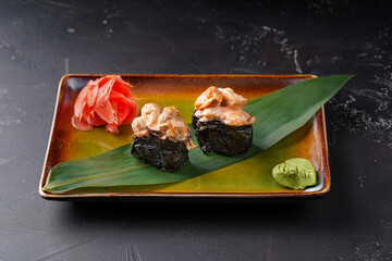 Gunkans with mussels on a plate are decorated with bamboo leaf wasabi and ginger on a dark background.