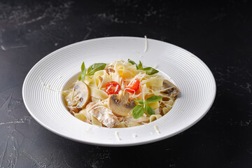Creamy pasta with mushrooms, chicken, basil, cheese and cherry tomatoes on a dark background.