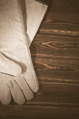 White leather welder gloves on a wooden background. A studio photo with hard lighting.