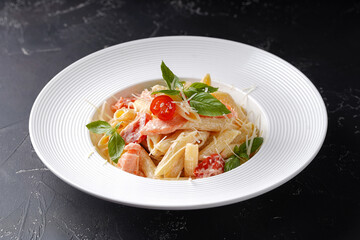 Creamy Penne pasta with salmon on a dark background in a white plate.